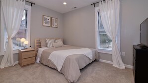 A bedroom with a bed, bedside tables, a lamp, curtains, and a TV stand.