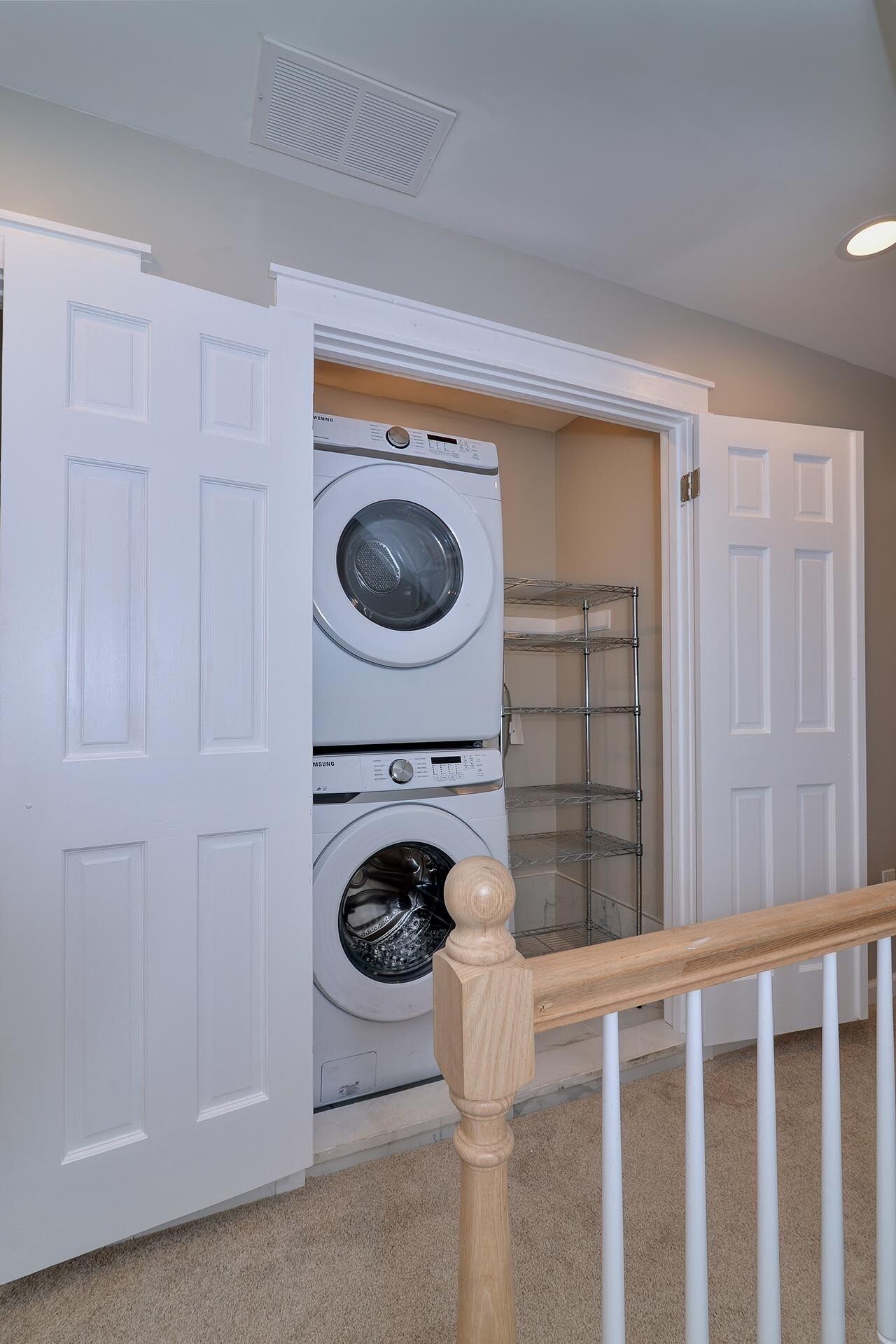 A laundry room with two stacked front-loading washing machines, a metal shelving unit, and a white door.