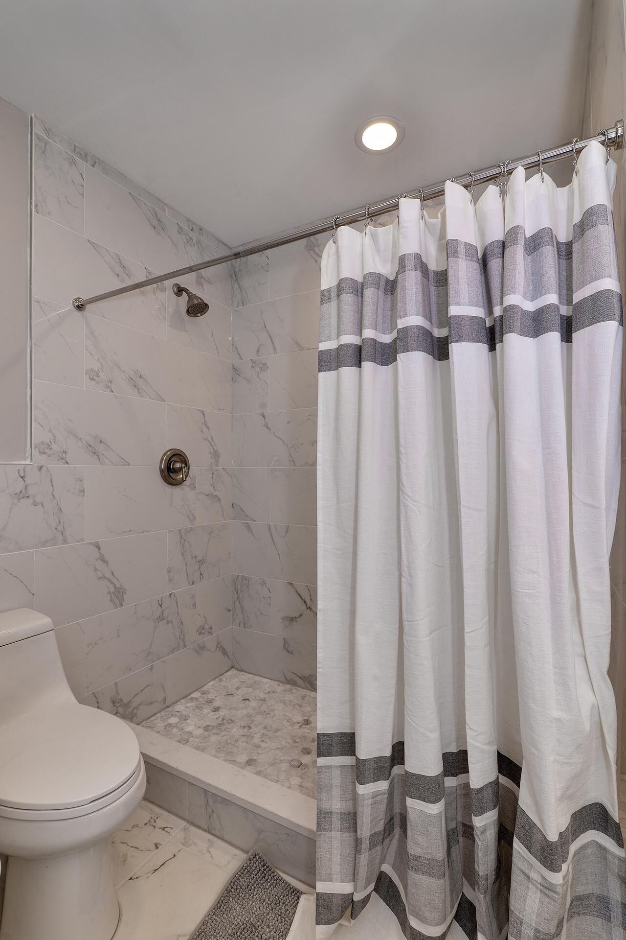 A bathroom with a shower, toilet, and marble tiles.