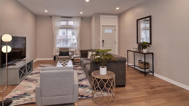 A modern living room with a sofa, ottoman, and a coffee table. There is a television, a lamp, and a plant on a side table.