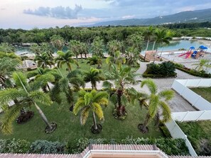 Stroll through the resort's lush garden, surrounded by palm trees and manicured lawns, with a swimming pool and slide nearby.