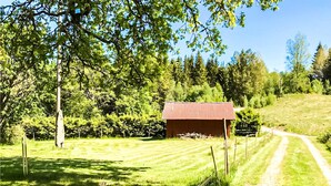 Un paysage rural avec une petite construction en bois, un chemin de terre et un champ d’herbe.