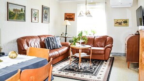 Un salon avec un canapé en cuir marron, une table basse ronde en bois et un tapis à motifs. On y trouve des tableaux encadrés au mur, une lampe et une plante en pot.