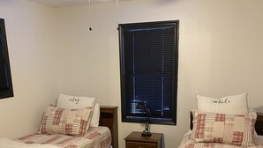 Habitació d'hotel amb dos llits, un ventilador de sostre, una taula de nit amb làmpada i una finestra amb persianes.