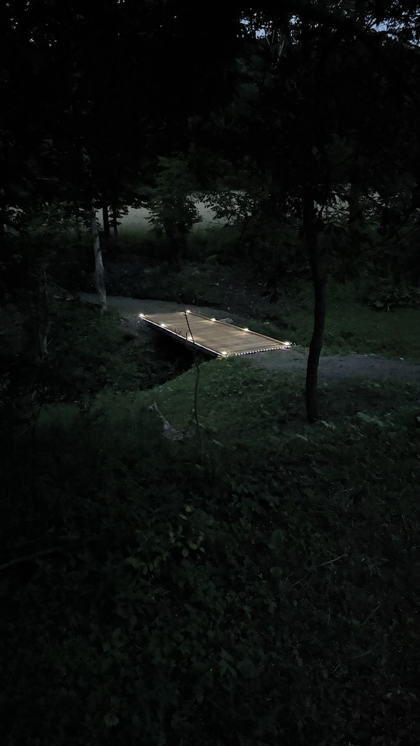 Un sentier menant à une petite structure illuminée, située dans une zone boisée.