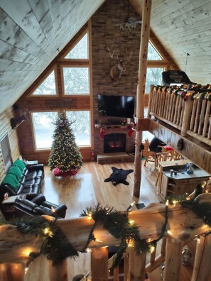 L’intérieur d’un chalet confortable en rondins de bois, avec une cheminée, un sapin de Noël, une tête de cerf empaillée et un téléviseur.