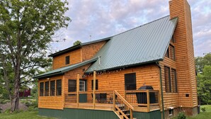 A log cabin with a green exterior, a wooden deck, and a chimney. - Cozy, country cabin near Cooperstown (Richfield Springs)