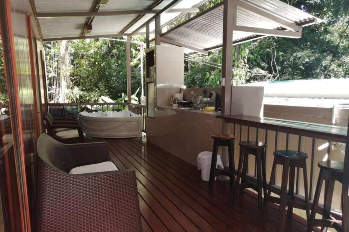 Et overdækket udendørs område med træterrasse, jacuzzi og bar med barstole.