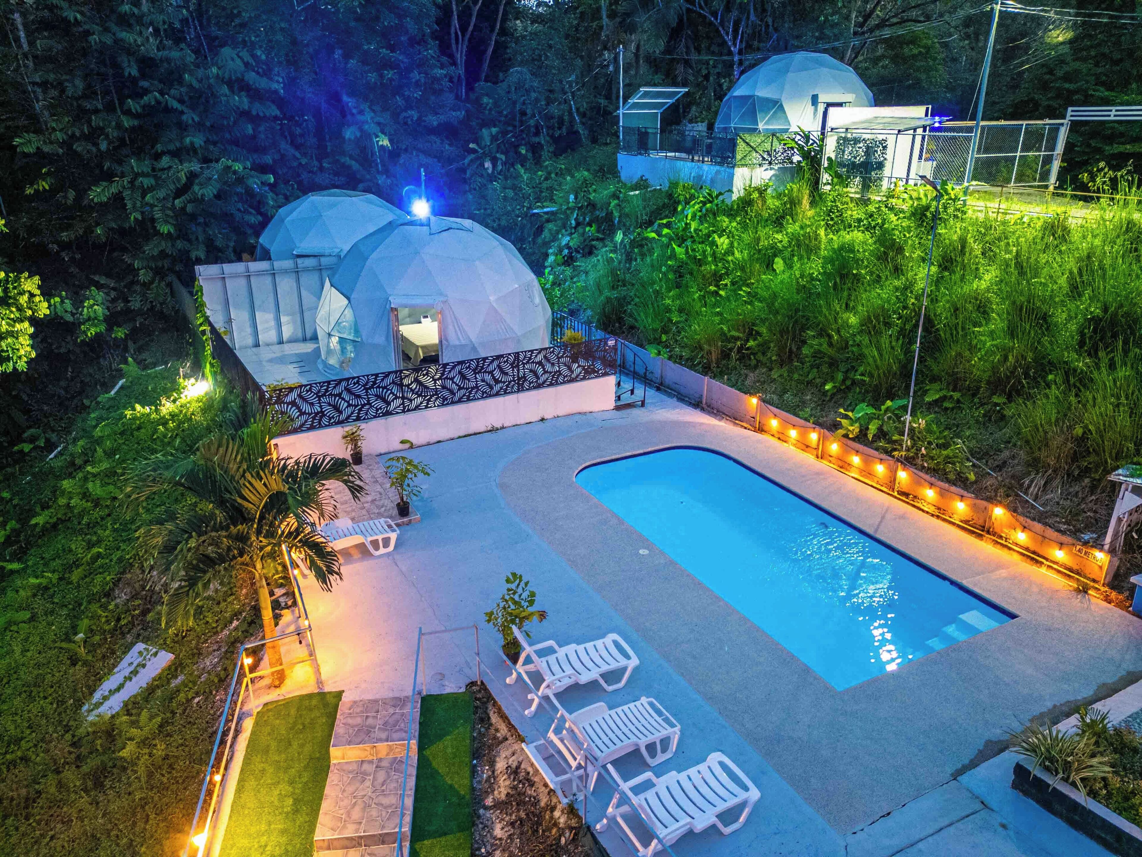 Una piscina con sillas de descanso, un pequeño jardín y dos estructuras en forma de cúpula.