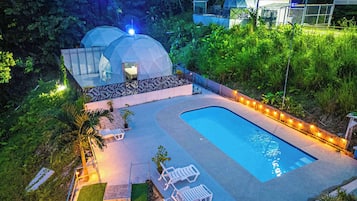Una piscina con sillas de descanso, un pequeño jardín y dos estructuras en forma de cúpula.