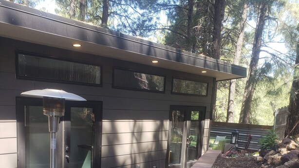 A modern outdoor patio with a grill, green chairs, and a stone wall. - The Tiny  Basecamp  (Flagstaff)