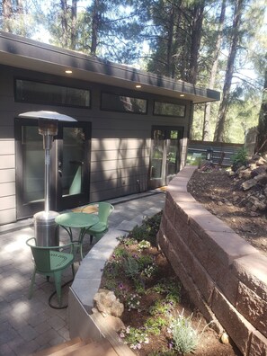 A modern outdoor patio with a grill, green chairs, and a stone wall.