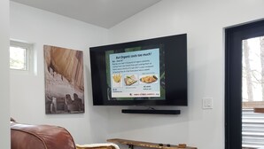 A modern living room with a leather sofa, a mounted TV, and a dining area with a wooden table and bench. - The Tiny  Basecamp  (Flagstaff)