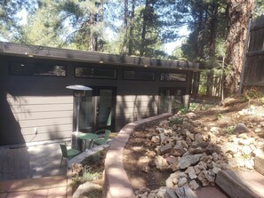 A modern building with a garage door, outdoor seating area with green chairs, and a landscaped garden with rocks and plants. - The Tiny  Basecamp  (Flagstaff)