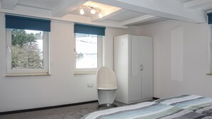 A bedroom with a bed, a wardrobe, a chair, and two windows with blinds. - Nice home in Medebach with sauna (Medebach)
