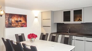 A modern kitchen with a white dining table and chairs, a vase of red flowers, and a painting above the table. - Nice home in Medebach with sauna (Medebach)
