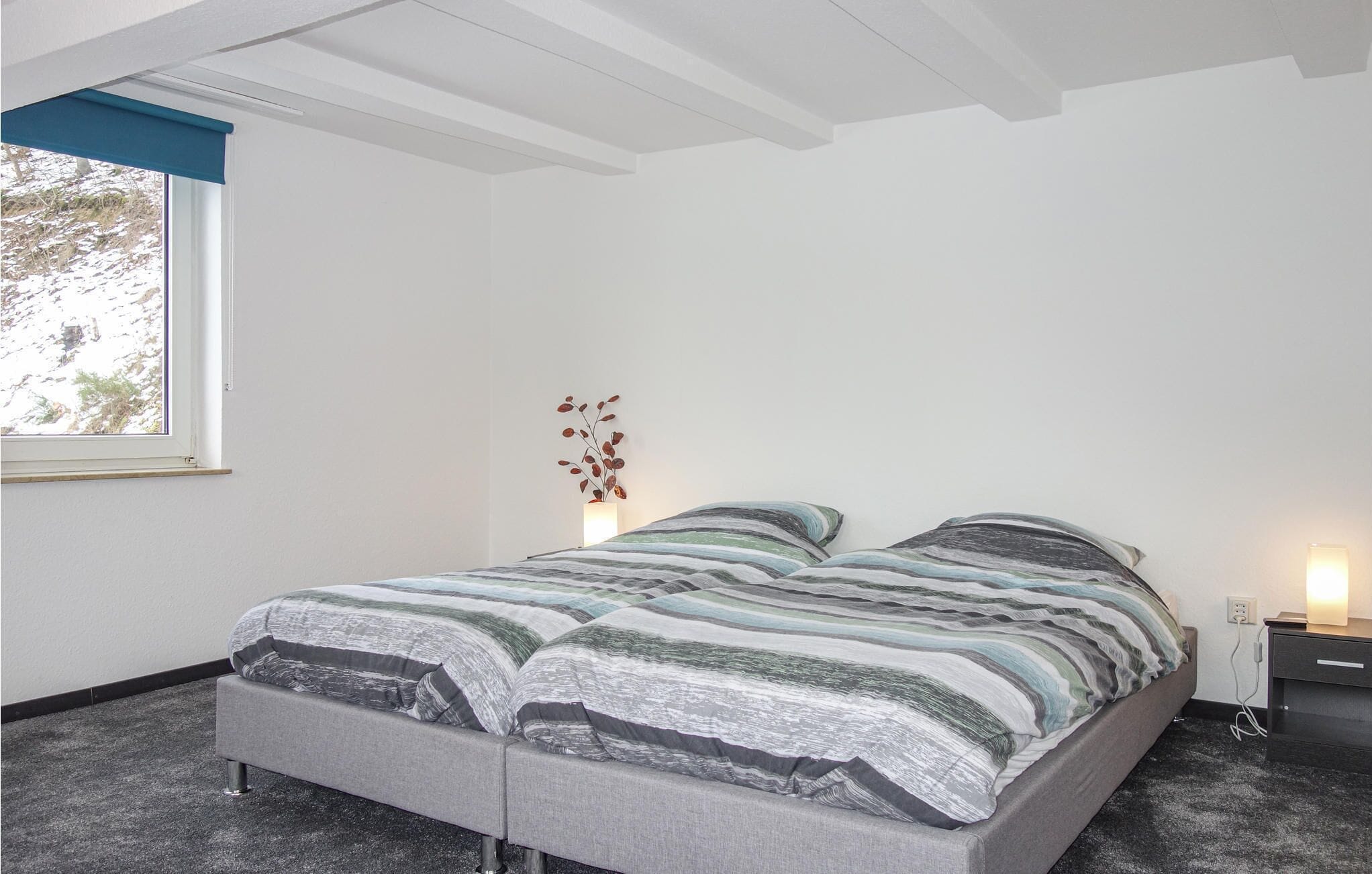 A bedroom with a bed, a nightstand, a lamp, and a window with a view of trees.