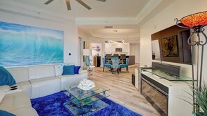 Un salon moderne avec un canapé blanc, une table basse en verre et un tapis bleu. On y trouve également un coin cuisine avec des meubles blancs et une table à manger avec des chaises.