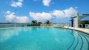 Une piscine d’un bleu éclatant, avec vue sur l’océan et des palmiers en arrière-plan.
