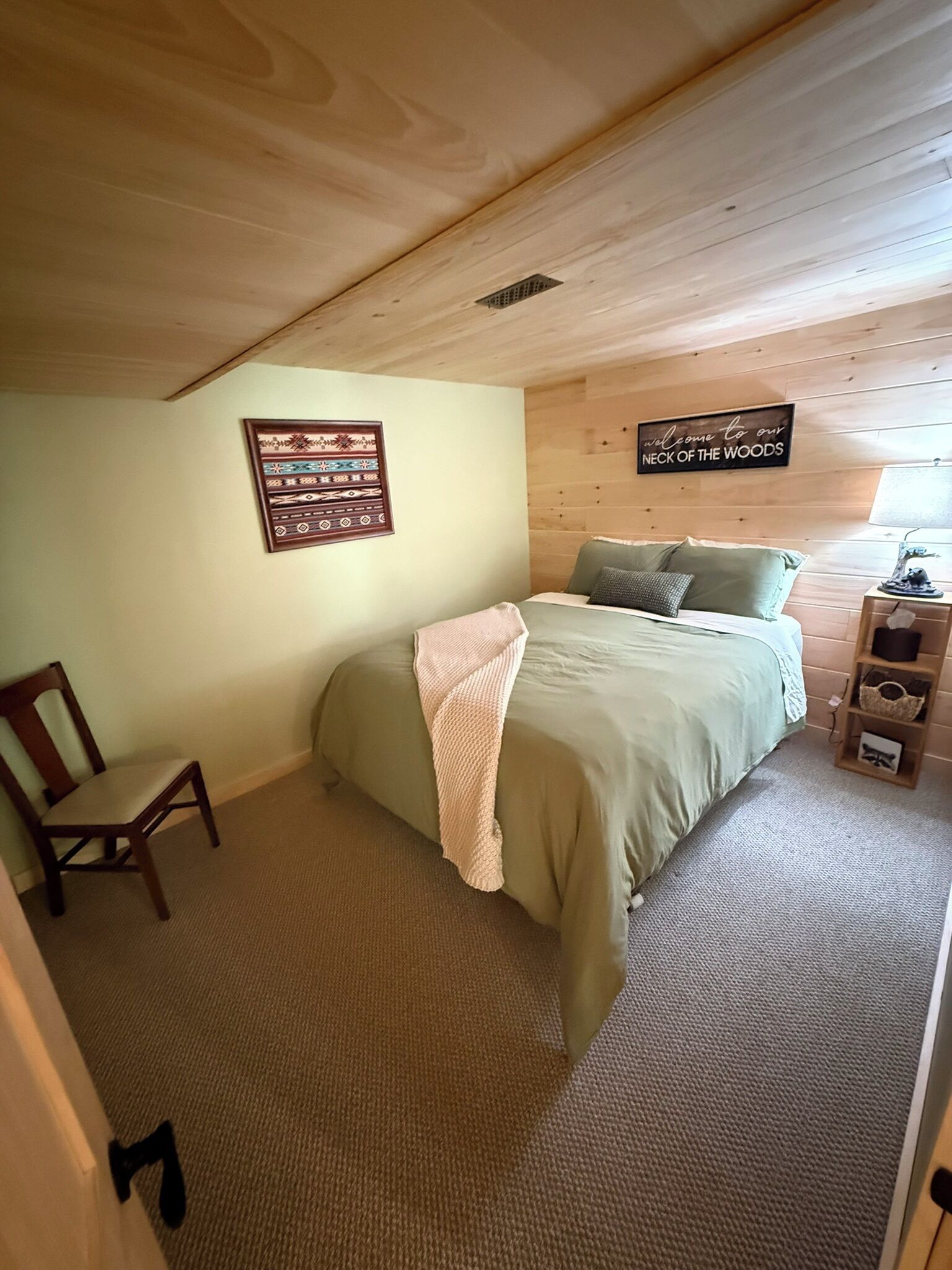 Een slaapkamer met een bed, een stoel, een houten hoofdbord, een wandbord en een plank met spullen.