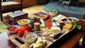 Een houten blokhut van binnen met een open haard, een houten terras en een tafel met verschillende soorten kaas, crackers en groenten.
