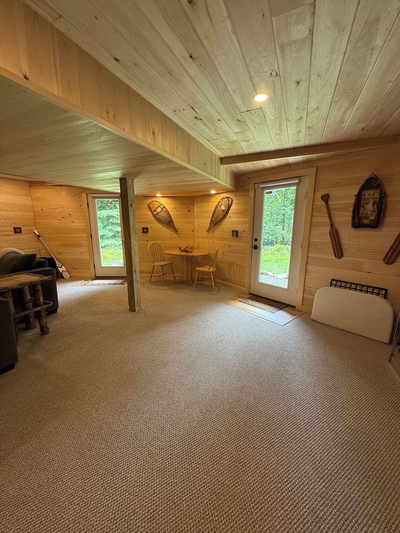 A log cabin interior with a carpeted floor, a dining table with chairs, and a wooden ceiling.