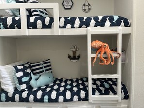 A bunk bed with nautical-themed bedding, a plush octopus toy, and a wall anchor decoration.