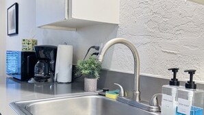 Et moderne køkken med en stålvask, kaffemaskine, en potteplante og dispensere til håndsæbe og opvaskemiddel.