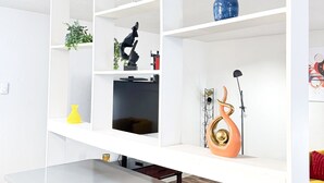 En moderne stue med et hvidt reolsystem, en sort sofa, et sofabord og en dekorativ skulptur.