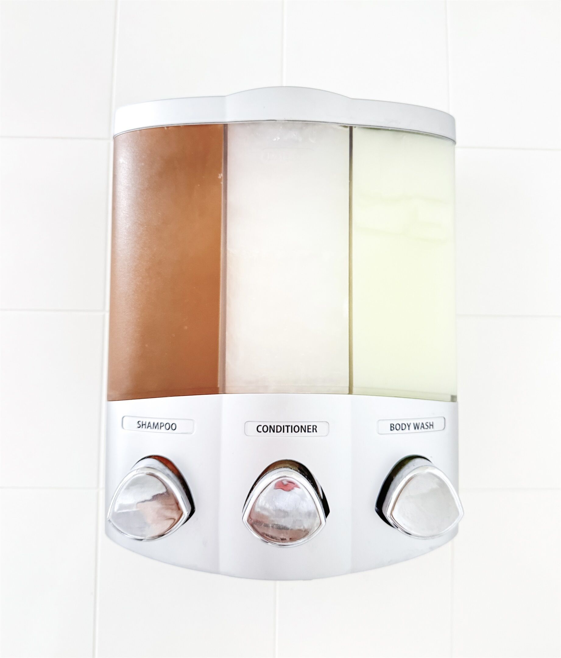 Panel de control de ducha empotrado en la pared, dividido en tres secciones etiquetadas para champú, acondicionador y gel de baño.