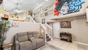 Een ruime woonkamer met een grijze bank, een trap en een muurschildering.