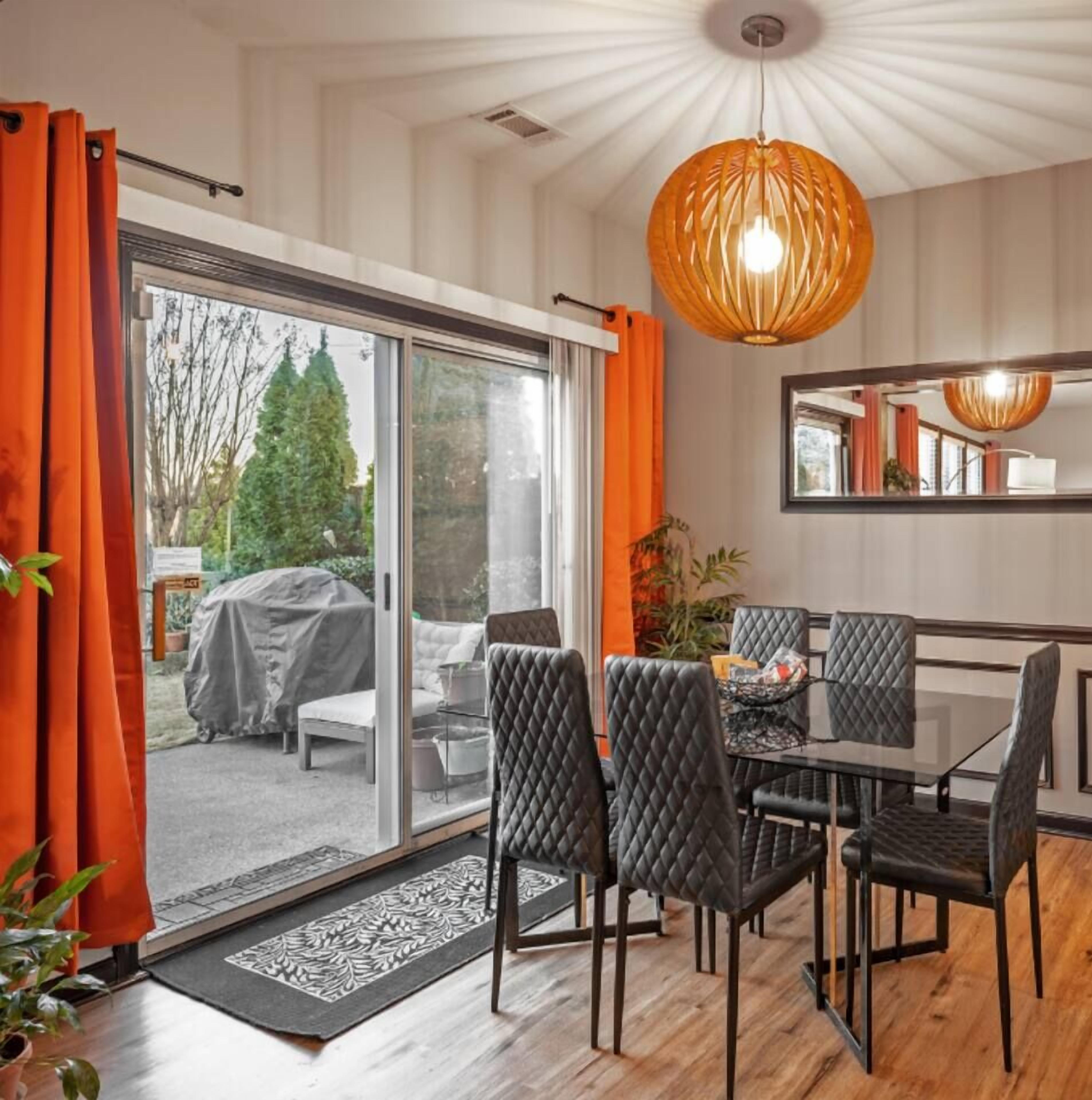 Un espace repas doté d’une porte vitrée donnant sur un coin salon extérieur abrité, une table à manger noire avec des chaises et un luminaire suspendu.