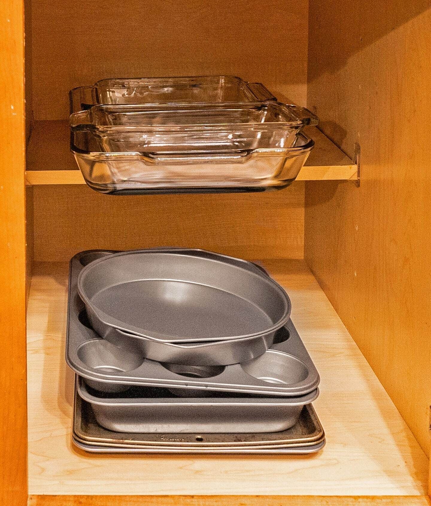 Une étagère de cuisine avec des plats de cuisson en verre transparent et une pile de poêles noires antiadhésives.