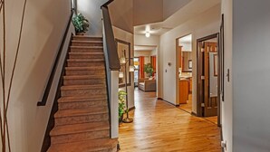 Una escalera conduce a una sala de estar con piso de madera, un sofá y un comedor, con una cocina al fondo.
