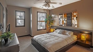 Un dormitorio con una cama, dos ventanas, un ventilador de techo y decoración en las paredes.