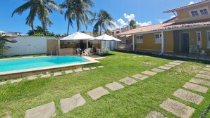 A sunny backyard with a swimming pool, palm trees, and a covered patio area.