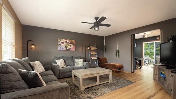 Un salon avec un canapé gris, une table basse, un ventilateur de plafond et un téléviseur.