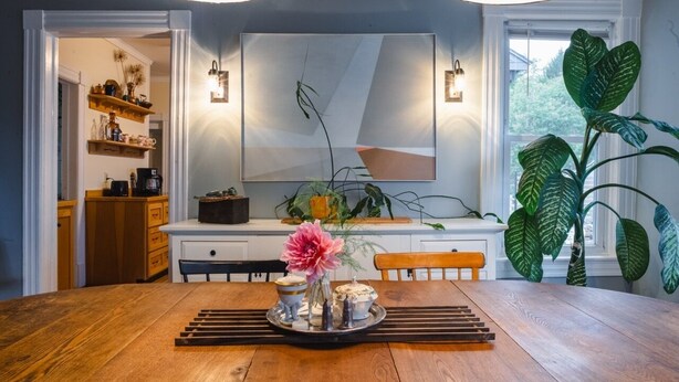 Un comedor con una mesa de madera, un jarrón con flores y una planta grande.