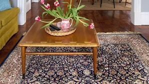 Una sala de estar con una mesa de centro de madera, un tapete estampado y un jarrón con flores rosadas.