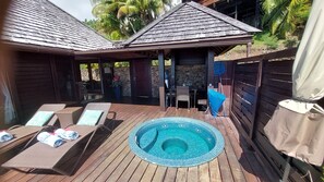 A wooden deck with a circular hot tub, lounge chairs, and a covered seating area.