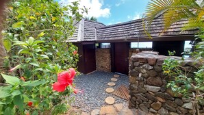 A stone-walled building with a wooden roof, a stone pathway, and lush greenery. - Stunning ocean & lagoon view in a completely renovated, entirely equipped villa (Haapiti)