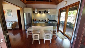 A modern kitchen with a central island, stainless steel appliances, pendant lighting, and a view to an outdoor deck. - Stunning ocean & lagoon view in a completely renovated, entirely equipped villa (Haapiti)
