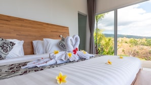 Ett hotellrum med en stor säng, prydligt bäddade vita sängkläder och utsikt över ett bergigt landskap genom stora fönster.