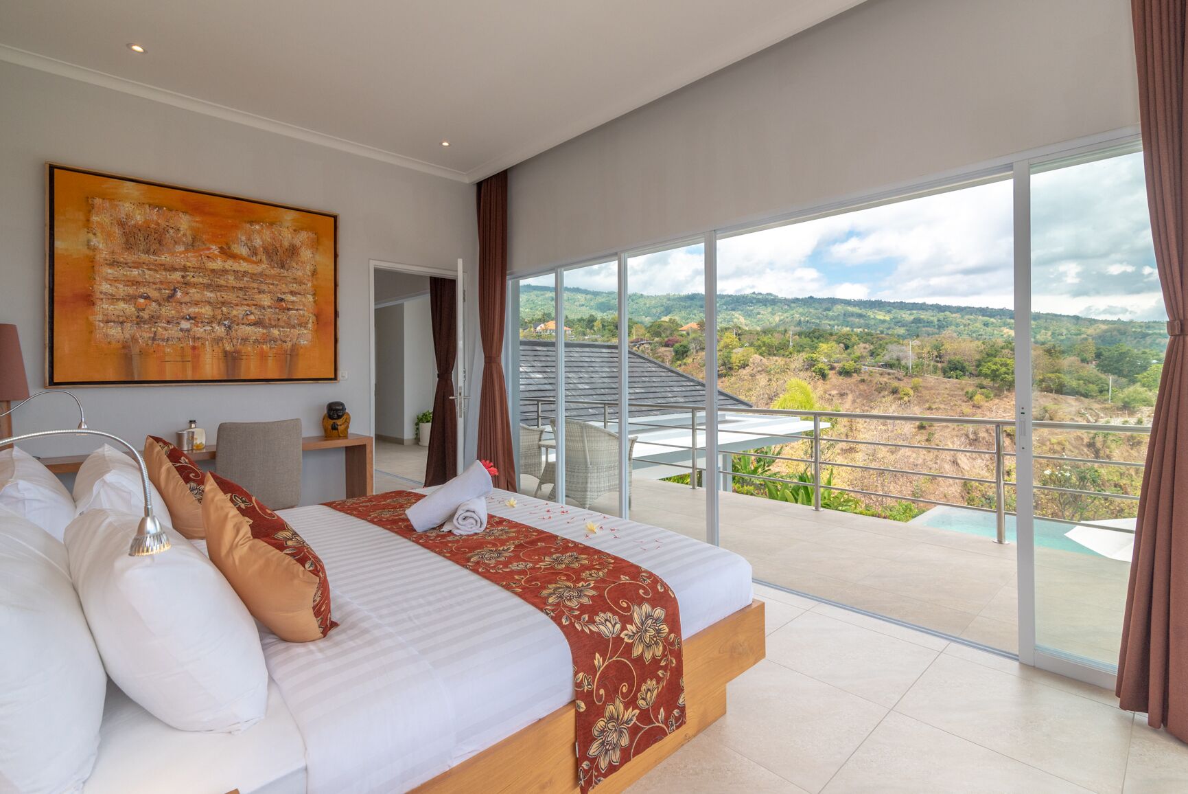 A bedroom with a large bed, a view of a mountainous landscape, and a balcony with a pool.