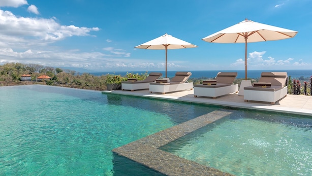 En infinitypool med solstolar och parasoller, med utsikt över ett vackert landskap.