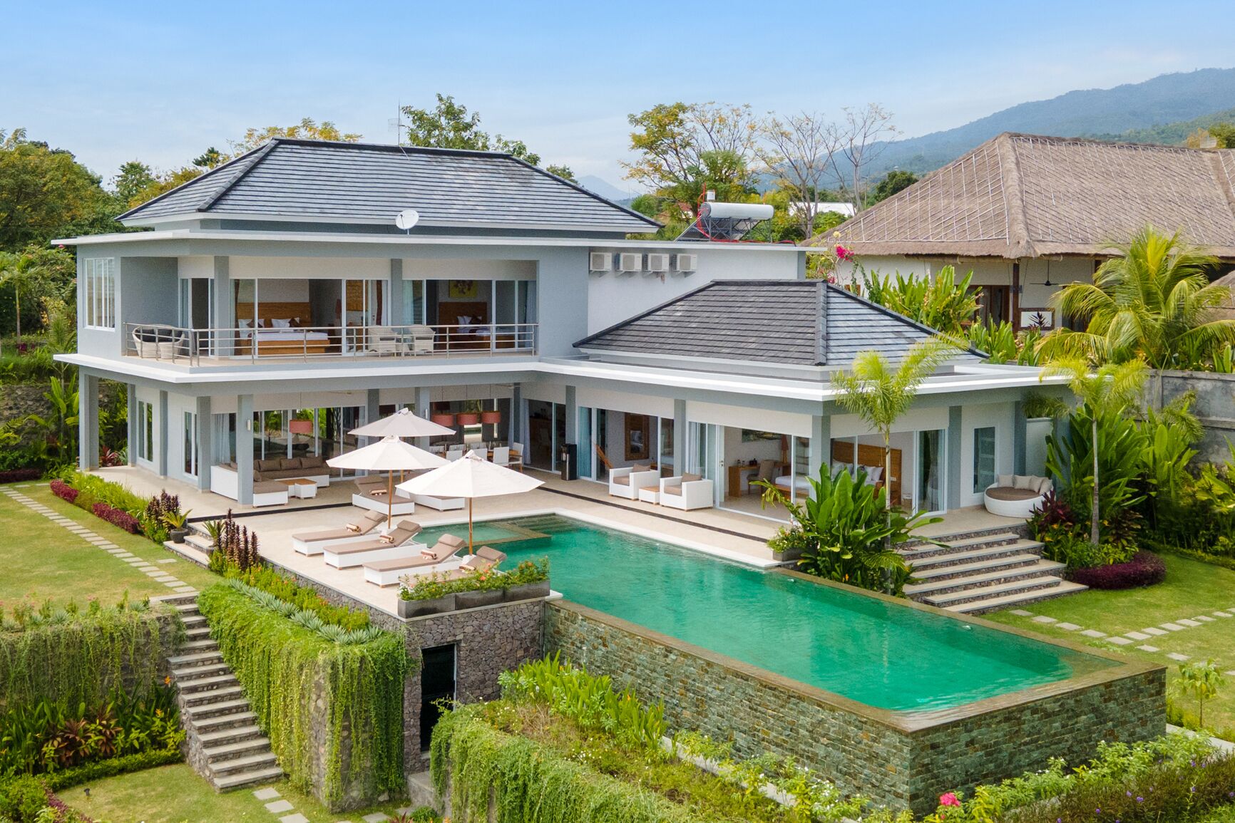 A two-story house with a swimming pool, outdoor seating, and lush landscaping.