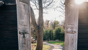Un cancello di legno aperto che dà su un sentiero in pietra, circondato da alberi e da un'area verde.