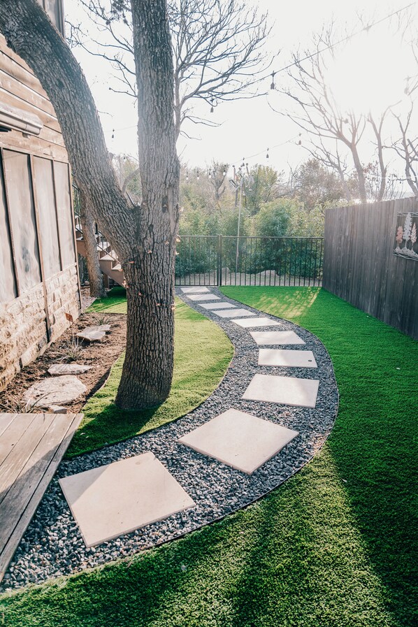 A curved stone pathway leading to a wooden deck, surrounded by a well-maintained lawn and a wooden fence.