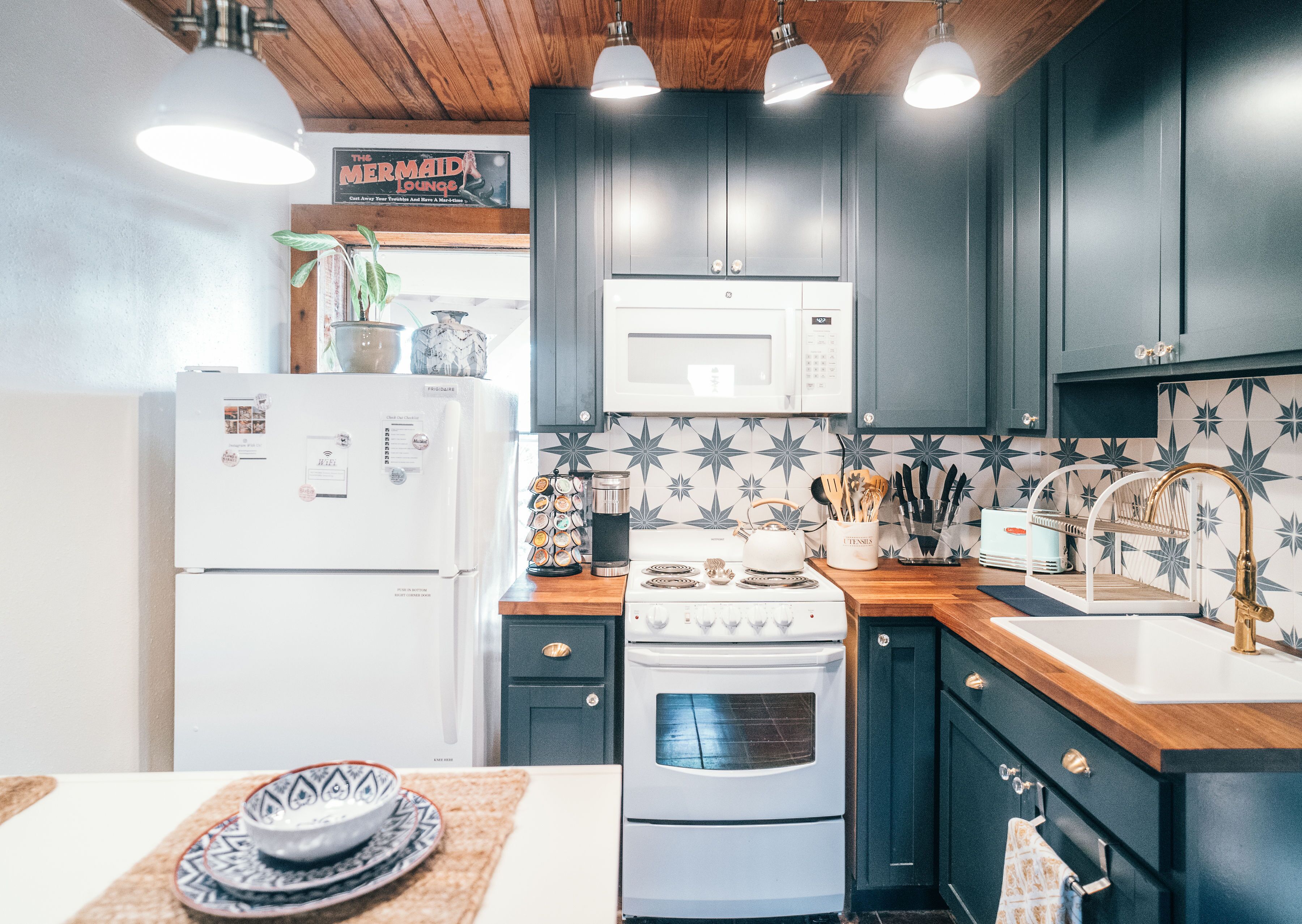 A kitchen with dark cabinets, a white refrigerator, a microwave, a stove, and a sink with a gold faucet.