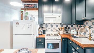 A kitchen with dark cabinets, a white refrigerator, a microwave, a stove, and a sink with a gold faucet.